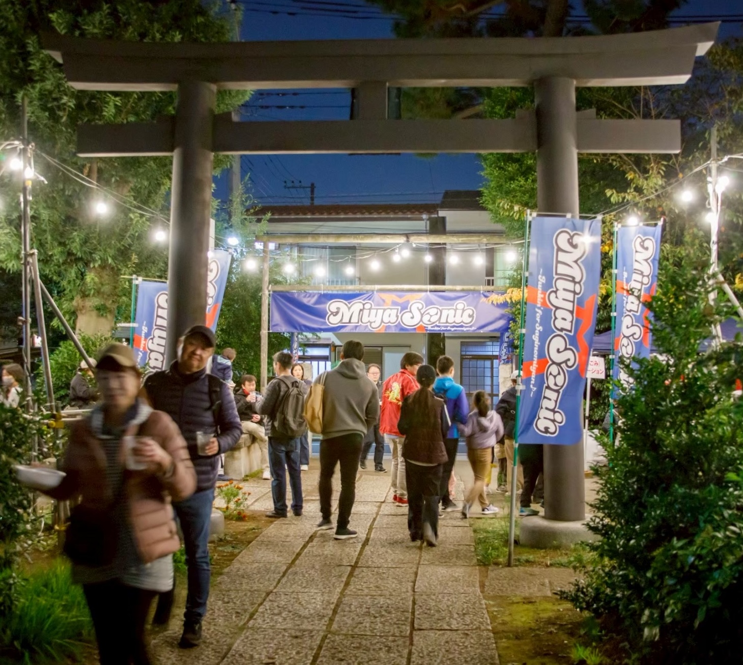 提灯が灯る夜の鳥居と会場へ向かう人々